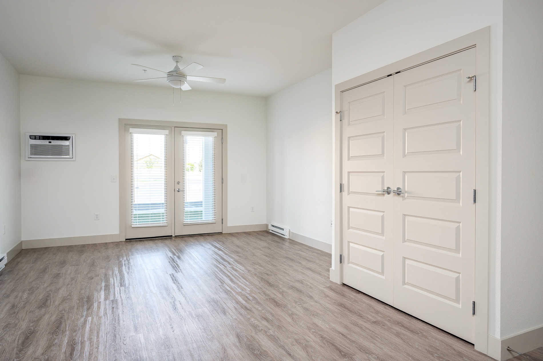 A room with a white door, a window with blinds, and a ceiling fan.